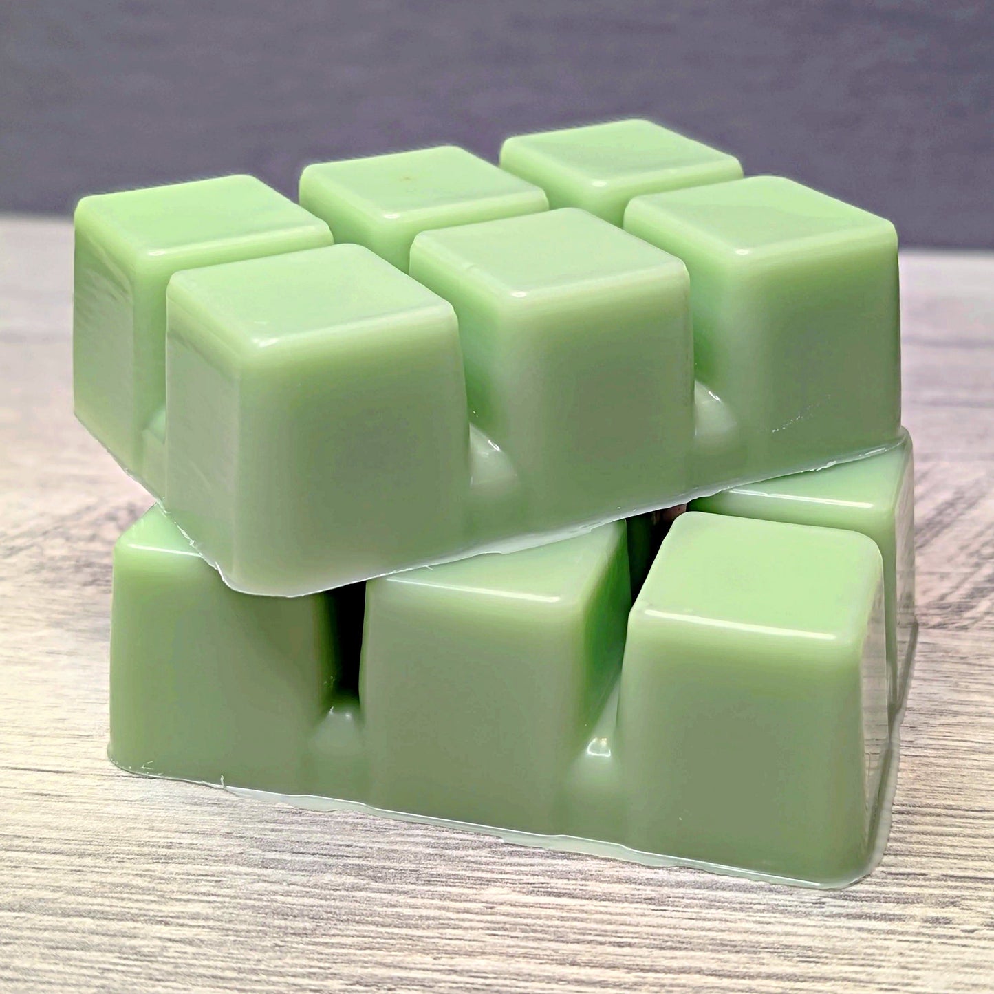 Stack of light green wax melt cubes on a wooden surface with a gray background