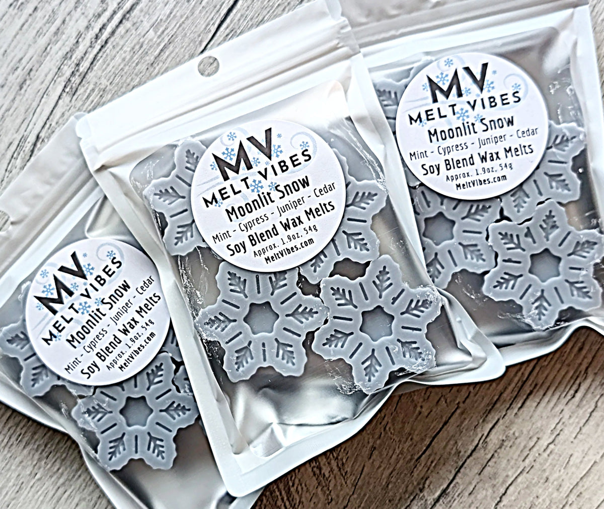 Three packages of Melt Vibes snowflake shaped wax melts on a wooden surface