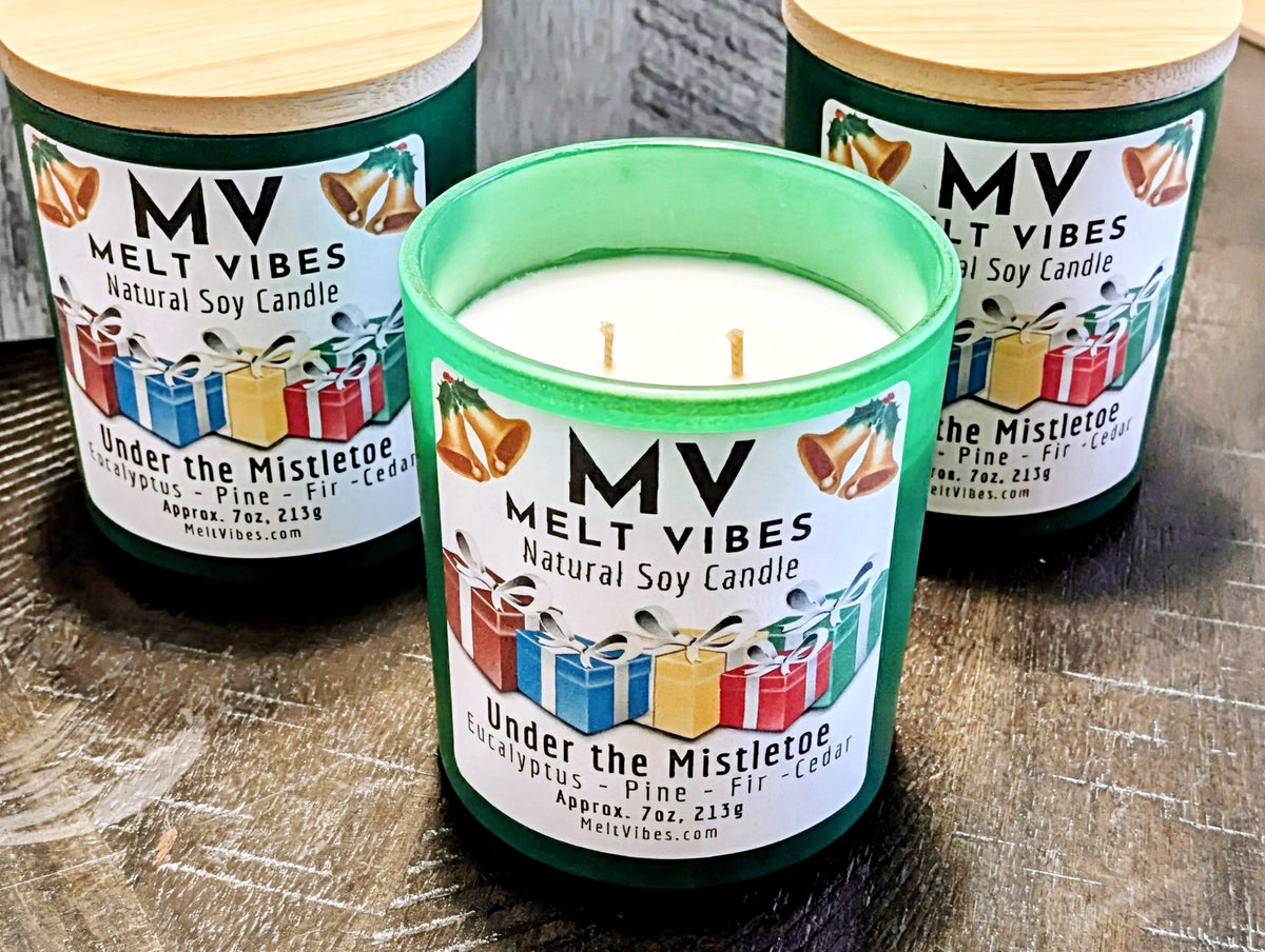 Three Melt Vibes 'Under the Mistletoe' natural soy candles in green glass jars with wooden lids, with one candle in the center open to show the white wax and wicks, set on a dark wooden surface.