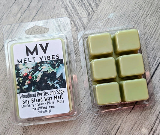 Two wax melts packages on a light wood surface: one sealed blister pack labeled MV Melt Vibes Woodland Berries and Sage, and one clear plastic tray holding six pale yellow wax cubes.