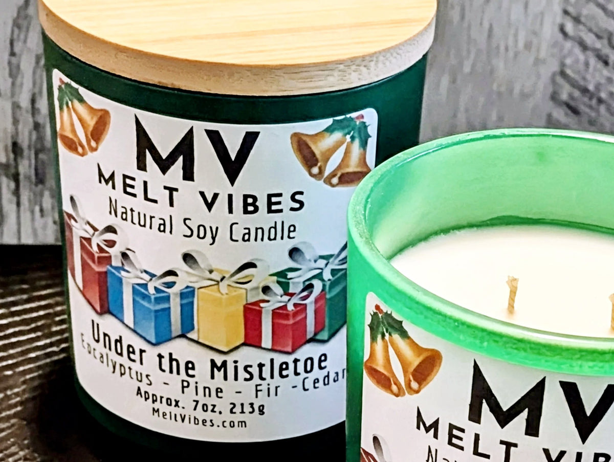 Two MV Melt Vibes natural soy candles shown close up. One candle has a dark green glass container with a light wood lid and a holiday-themed label.