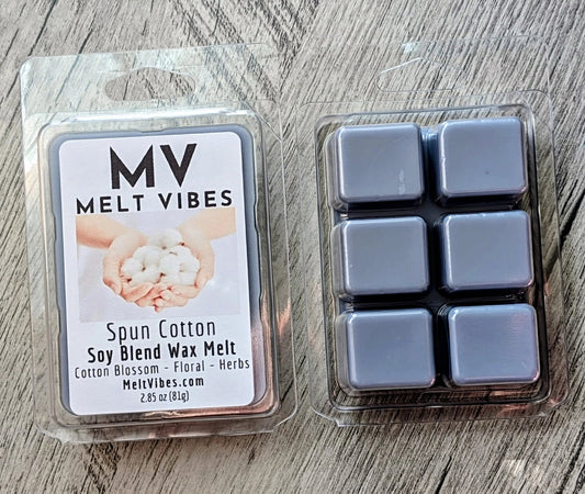 Two packages of MV Melt Vibes Spun Cotton soy blend wax melt on a gray wood background. One package shows the white front label, and the other shows six gray wax melts inside a clear plastic tray.