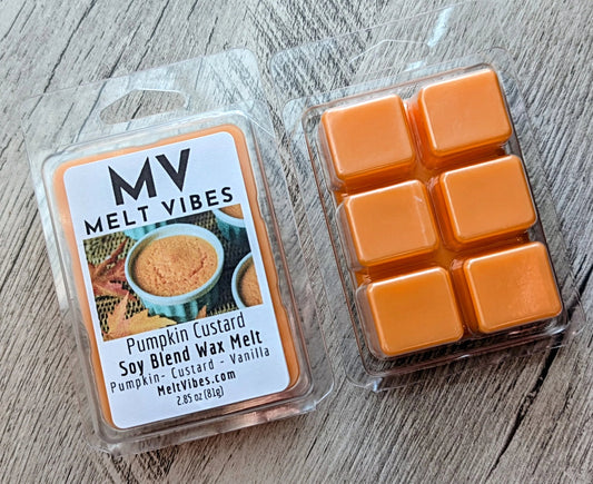 Two packages of MV Melt Vibes Pumpkin Custard soy blend wax melt on a gray wood background. One package shows the front label, and the other shows six orange wax melts in a clear plastic tray.